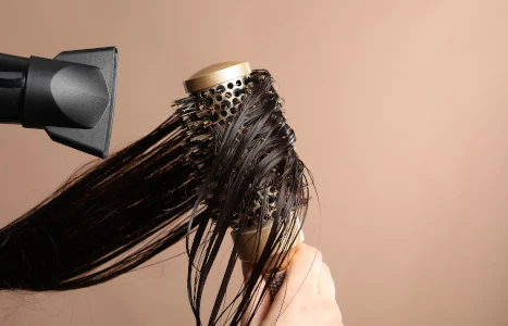 Eine Hand hält eine nasse Lockenbürste unter einen Haartrockner während feuchtes Haar herausgeschüttelt wird