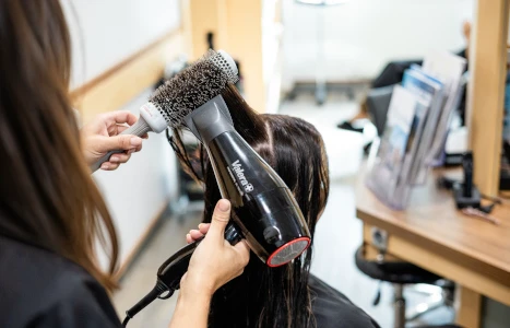 Eine Hand hält eine nasse Lockenbürste unter einen Haartrockner während feuchtes Haar herausgeschüttelt wird