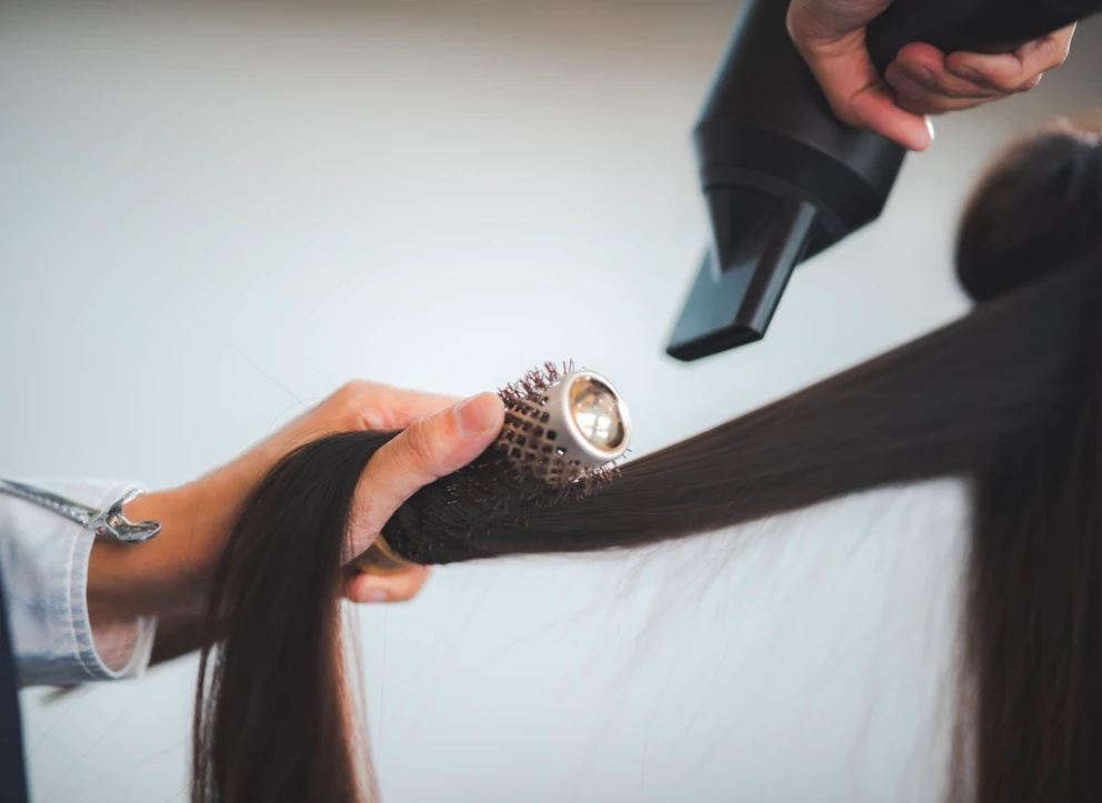 Eine Hand hält das Haar während ein Stylist einen Föhn verwendet um es zu trocknen
