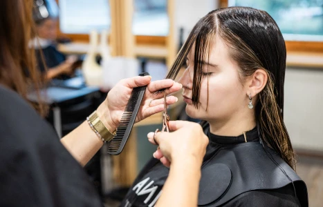 Ein Stylist schneidet mit Scheren einen Haarspitzenrand eines Kunden